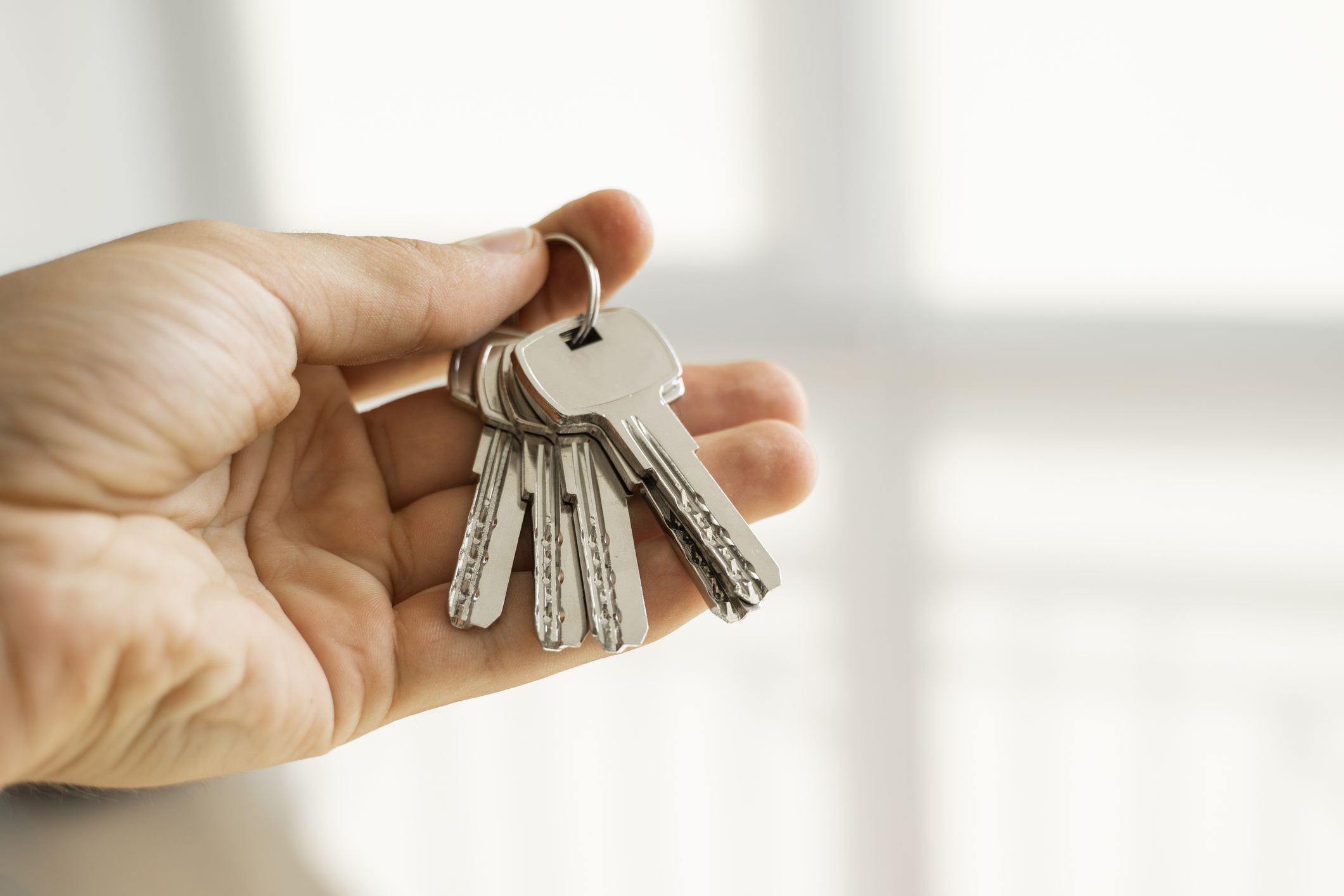 Mens hand holding a set of keys. Real Estate Agent is giving the keys to an apartment to clients. Focus on the keys. Bunch of keys in a Real Estate Agents hand.